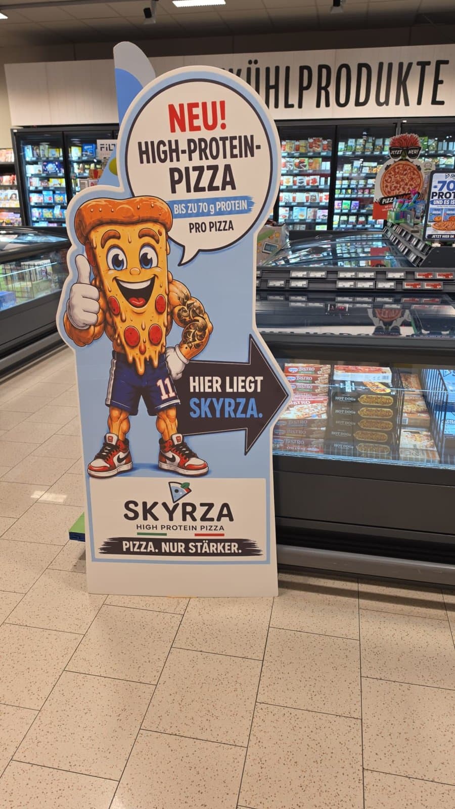 SKYRZA-Aufsteller mit Pizza-Figur neben der Tiefkühltruhe